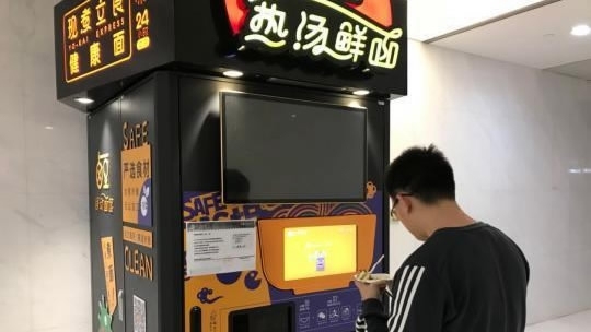 A customer waits for his noodles in front of a noodle vending machines. [File Photo: CGTN] 