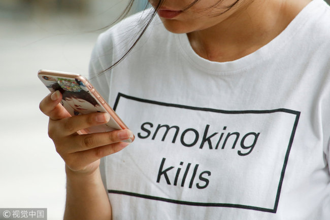 A woman wearing a "smoking kills" T-shirt uses a mobile phone in Beijing, June 3, 2017. [File Photo: VCG]
