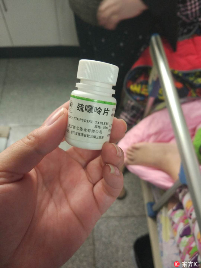 The mother of a young leukemia patient holds a bottle of mercaptopurine tablets from overseas. [Photo: Imagine China]