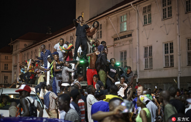 Zimbabweans drink, dance, sing and ride on a passing truck as they celebrate at night after hearing the news that President Robert Mugabe had resigned, in downtown Harare, Zimbabwe Tuesday, Nov. 21, 2017. [Photo: IC]