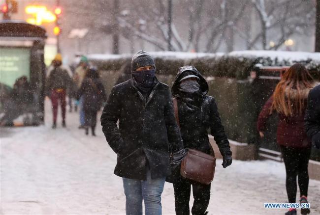 People walk in the snowfall in downtown Chicago, the United States, Dec. 29, 2017. [Photo by Xinhua]