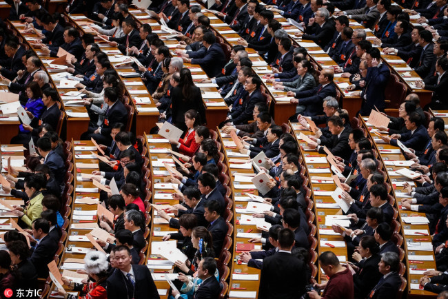 Delegates check their ballot tickets during the third plenary session of the 13th National People's Congress (NPC) at the Great Hall of the People in Beijing on March 11, 2018. [Photo: IC]