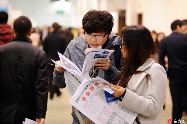 Two job hunters read employment information at a job fair in Hangzhou, east China's Zhejiang Provinc, on Mar. 17, 2015. [File Photo: IC] 