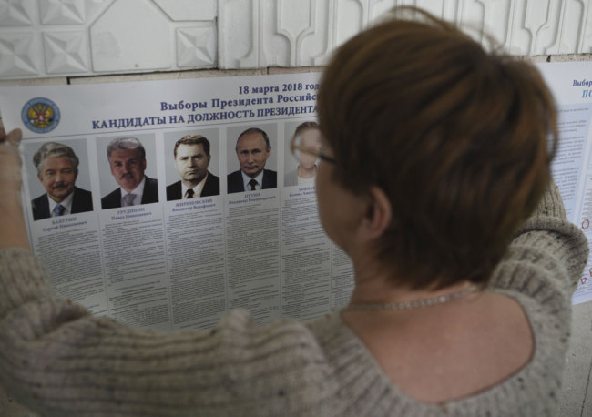 A polling station official hangs a list of candidates for the 2018 Russian presidential election, during preparations for the 2018 Russian presidential election at a polling station in Simferopol, Crimea, Saturday, March 17, 2018. Russian voters, observers and eight presidential candidates are gearing up for an election that will undoubtedly hand Vladimir Putin another six-year term. [Photo: AP]