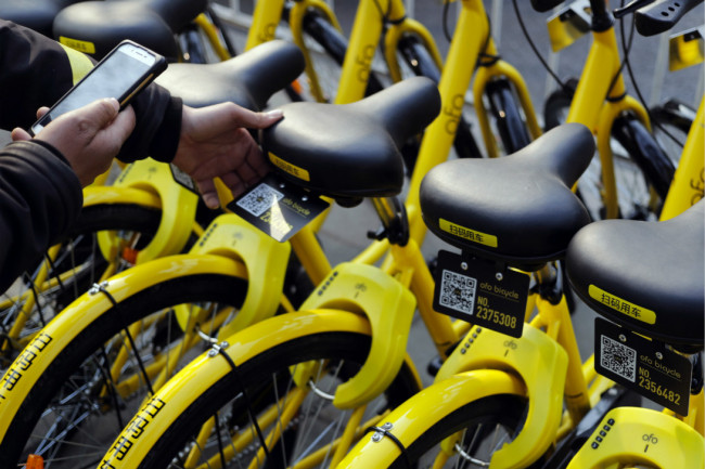 A man uses the bike-sharing application on his smartphone to unlock the bicycle from bike-sharing company Ofo parked on the sidewalk in Beijing, China. [Photo: AP]