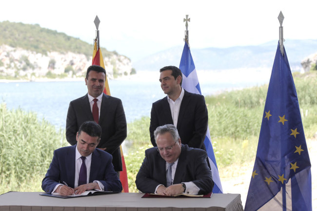 Greek Prime Minister Alexis Tsipras, background right, and his Macedonian counterpart Zoran Zaev, background left, look on as Greek Foreign Minister Nikos Kotzias, right, and his Macedonian counterpart Nikola Dimitrov sign an agreement on Macedonia's new name in the village of Psarades, Prespes Greece, on Sunday, June 17, 2018. [Photo: AP/Yorgos Karahalis]