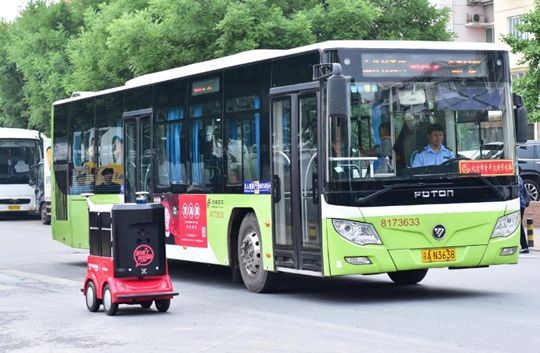 A JD.com automatic delivery vehicle waits at a red light alongside a bus in Haidian district, Beijing, during a trial run in this undated photo. [Photo: Xinhua]