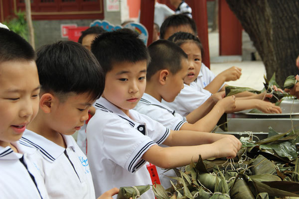 Primary school students learn to wrap up Zongzi at a cultural event held in Beijing Folklore Museum to celebrate the Dragon Boat Festival. Zongzi is a glutinous rice pudding with various fillings wrapped in bamboo or reed leaves, and is often eat during the Dragon Boat Festival. [Photo: China Plus/Zhu Yan]
