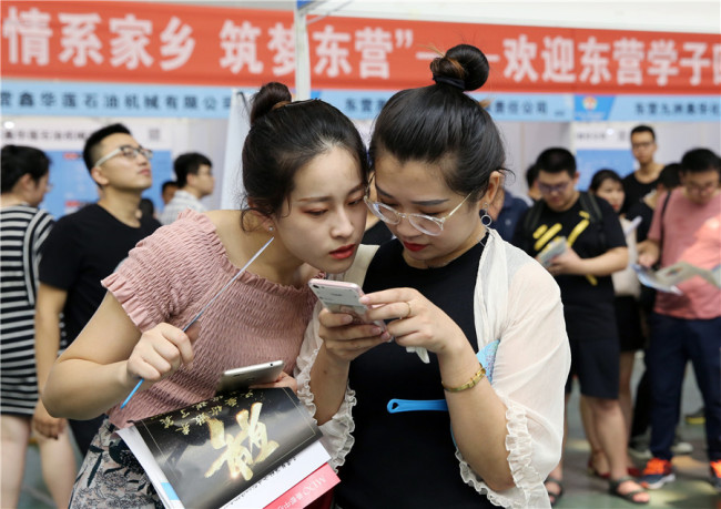 Job seekers share employment information at a job fair in Dongying, Shandong province, on July 15. [File Photo: China Daily]