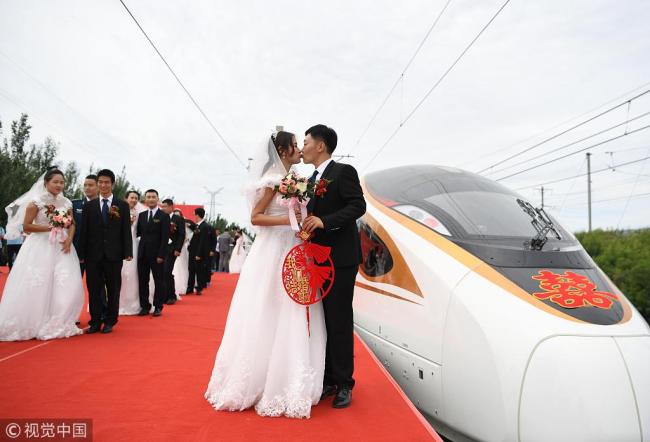 The newlyweds kiss in front of a Fuxing bullet train in Changchun, Jilin Province on August 18. [Photo: VCG]