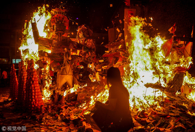 A woman throws prayer paper onto a fire during celebrations for the Ghost Festival in Kuala Lumpur, Malaysia on August 6, 2016. [File Photo: VCG]
