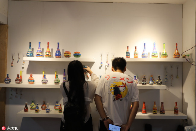 Customers look at paintings with colored sand in glass bottles made by An Nike at the shop. [Photo/IC]