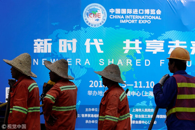 Workers stand in front of a billboard promoting the upcoming China International Import Expo in Shanghai, China September 27, 2018. [Photo: VCG]