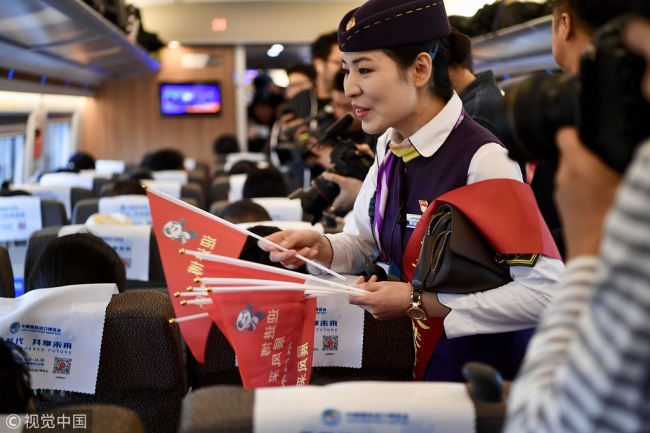 A train attendant hands out flags featuring the expo mascots, on a CIIE-themed train at Shanghai Hongqiao Railway Station on Wednesday, October 10, 2018. [Photo: VCG]