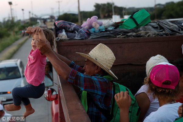 A migrant, part of a caravan traveling en route to the United States, helps a child to board a truck, as they hitch a ride on the truck, in Santo Domingo Ingenio, Mexico, on November 8, 2018. [Photo: VCG]