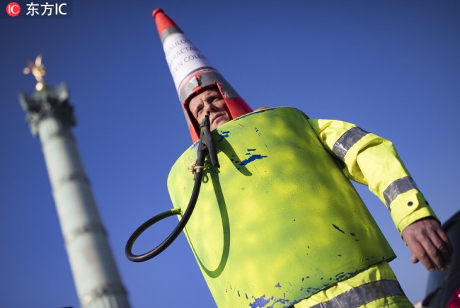 A man wearing a costume symbolizing a petrol pump, painted high-visibility yellow, like the mandatory high-visibility yellow vests in cars which has become a symbol of French driver's and citizen's protest against higher fuel prices, on Place de la Bastille as protesters try to block roads and cause traffic disruptions as part of a nationwide protest, in Paris, France, November 17, 2018.[Photo: IC]