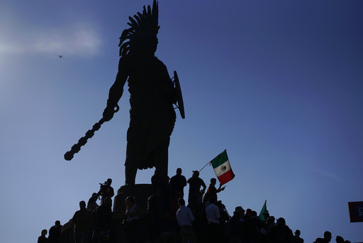 Demonstrators stand under an indigenous statue of Aztec ruler Cuauhtemoc as they protest the presence of thousands of Central American migrants in Tijuana, Mexico, Sunday, Nov. 18, 2018. [Photo: AP]