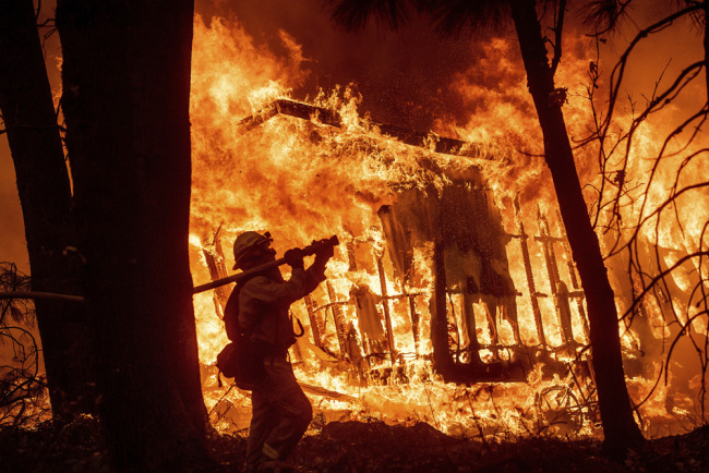 In this Nov. 9, 2018 file photo, firefighter Jose Corona sprays water as flames from the Camp Fire consume a home in Magalia, Calif. A massive new federal report warns that extreme weather disasters, like California’s wildfires and 2018’s hurricanes, are worsening in the United States. [Photo: AP]