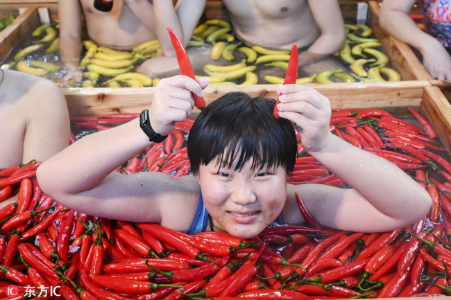 A visitor poses(摆姿势 bǎi zīshì) amongst chilli peppers in the nine-grid hotpot-shaped hot spring pool filled with vegetables and fruits at a hotel in Hangzhou, east China's Zhejiang Province, January 27, 2019. [Photo: IC]