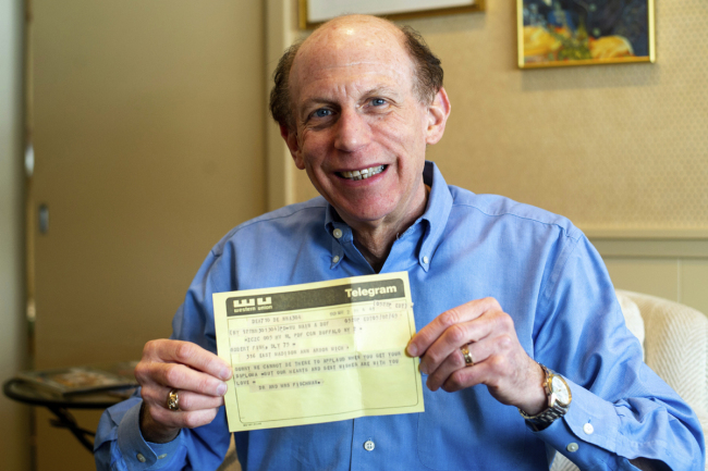 In a Friday, March 1 2019 photo, Robert Fink holds up a telegram from a family friend congratulating him on his 1969 graduation from the University of Michigan at his home in Huntington Woods, Mich. The telegram, delivered to his apartment the day after he moved away from Ann Arbor, was recovered 50 years later by an employee of a downtown Ann Arbor company in a filing cabinet bought from the University of Michigan. [Photo: Ann Arbor News via AP/Jacob Hamilton]