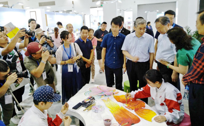 China's Minister of Culture and Tourism Luo Shugang and Deputy Minister Xiang Zhaolun along with officials from the Beijing municipal government visit the booth for the High School Affiliated to Renmin University of China during the fourth Beijing-Tianjin-Hebei Intangible Cultural Heritage Exhibition. The students were making "Cao's kites" at the event in Beijing in June 2018. Cao's kite is named after Cao Xueqin, the author of Chinese classic "Dream of the Red Chamber". [Photo provided to China Plus]