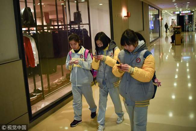 Students use their mobile phones as they walk through a mall in Beijing. [File Photo: VCG]