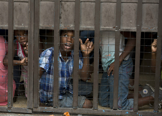 A migrant child calls out to a street vendor selling water as he waits with other children inside an area of the Mexican Commission for Refugee Aid office, while their parents fill out paperwork, in Tapachula, Mexico, Friday, April 26, 2019. Thousands of migrants remain on the southern border of Mexico waiting for documents that allow them to stay legally in the country. [Photo: AP/Moises Castillo]