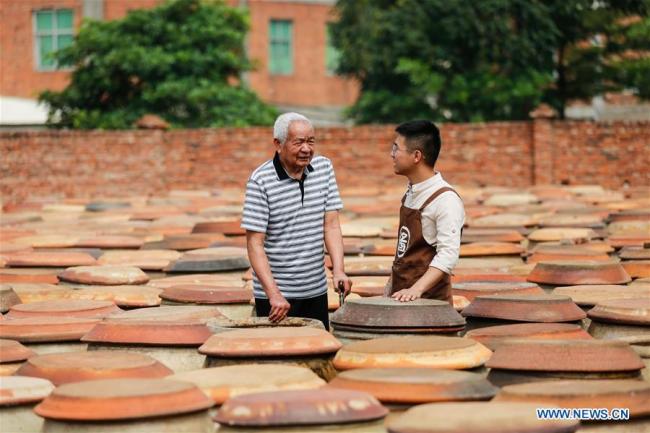 Wu Huaqing learns(学习 xuéxí) from his grandfather Wu Zongzhong among soy sauce jars at his company in Quanzhou, southeast China's Fujian Province, April 29, 2019.[Photo: Xinhua]
