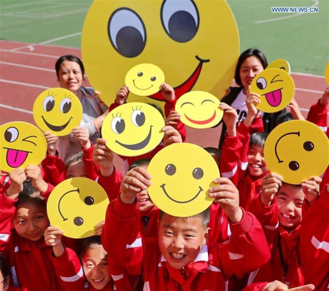 Pupils(学生们 xuéshēngmen) demonstrate smiley cards(卡片 kǎpiàn) to greet the upcoming World Smile Day at a primary school in Qinhuangdao, north China's Hebei Province, May 7, 2019. [Photo: Xinhua]