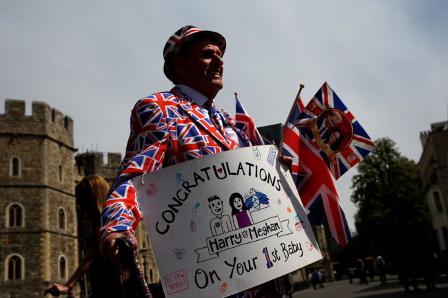 A royal super fan wearing a Union-flag themed suit holds a congratulatory banner as he walks outside Windsor Castle in Windsor, west of London on May 7, 2019, the day after the announcement that Britain's Meghan, Duchess of Sussex had given birth to a son. [Photo: AFP]