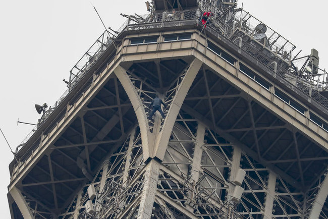 A man (C) climbs up to the top of the Eiffel Tower, in Paris, without any protection as a firefighter (R) looks down at him from the top, on May 20, 2019. [Photo: AFP/Francois Guillot]