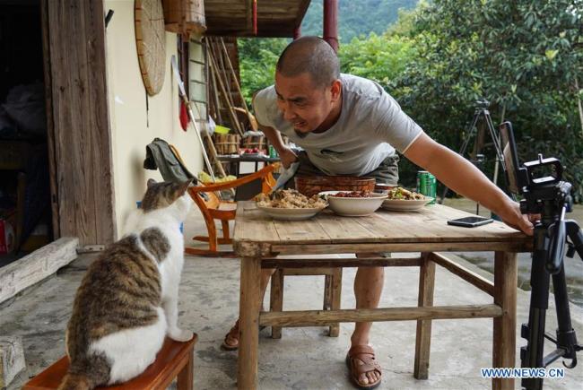 Jiang Jinchun interacts(互动 hùdòng) with his cat at home during his live broadcast in Zaotian Village in Hengfeng County, east China's Jiangxi Province, June 19, 2019. [Photo: Xinhua]