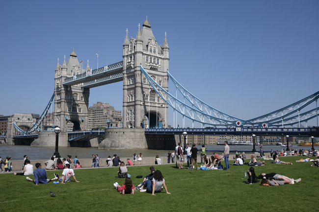 In this file photo taken on May 26, 2017 People relax in the hot and sunny weather on the grass beside Tower Bridge and the river Thames in London. London's iconic Tower Bridge celebrates its 125th anniversary on Sunday by showing off the weird and wacky alternative designs that were nearly built instead. [Photo: AFP/Daniel LEAL-OLIVAS]