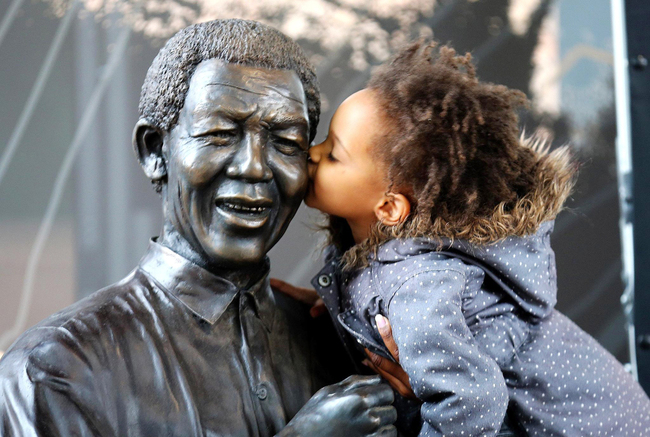 A young girl kisses a statue of former South African President Nelson Mandela before a service conducted by Archbishop Desmond Tutu at the Nelson Mandela Foundation on December 9, 2013 in Johannesburg, South Africa. [File photo: VCG]