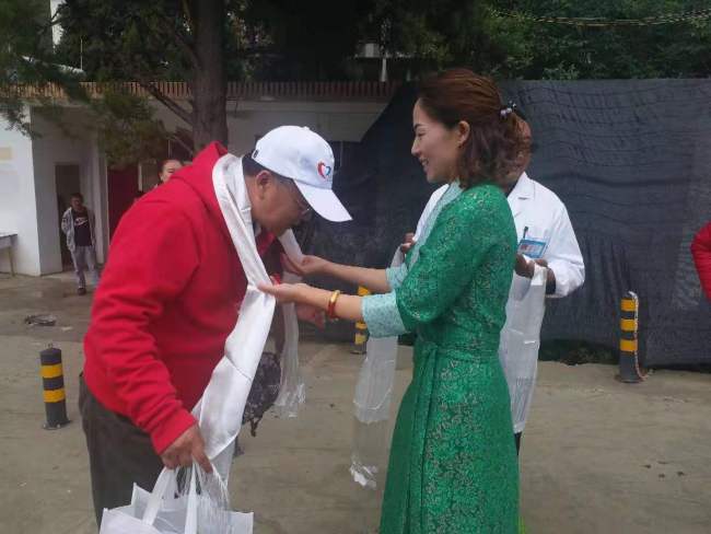 A representative from Tuoding Township presents hada, a white silk scarf, to a voluntary doctor to show respect and blessings. [Photo: China Plus]