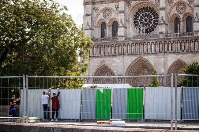 Workers install protection panels as police officers secure a perimeter around the Notre Dame Cathedral ahead of the start of a massive anti lead decontamination treatment around the monument, in Paris, France, 13 August 2019. [Photo: IC]