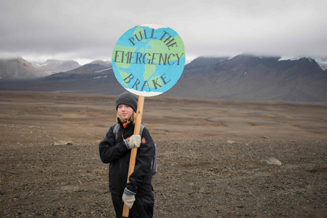 An Icelandic girl poses for a photo with a "Pull the emergency brake" sign near to where a monument was unveiled at the site of Okjokull, Iceland's first glacier lost to climate change in the west of Iceland on August 18, 2019. [Photo: AFP via VCG/Jeremie Richard]