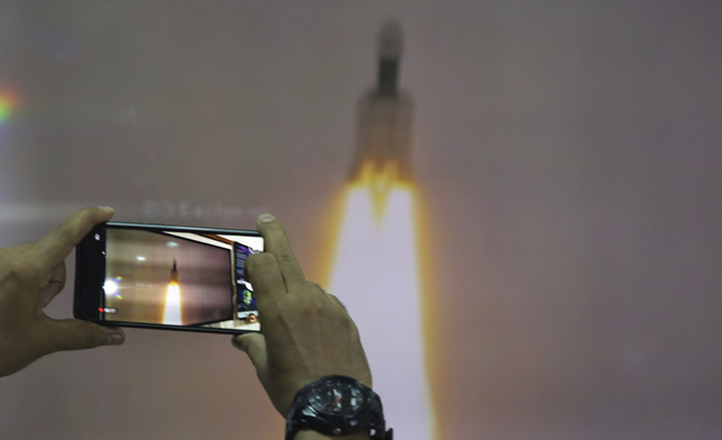 A man at New Delhi's Nehru Planetarium, takes pictures of a web cast of the lift off of Indian Space Research Organization (ISRO)'s Geosynchronous Satellite launch Vehicle (GSLV) MkIII carrying Chandrayaan-2 from Satish Dhawan Space center in Sriharikota, India, Monday, July 22, 2019. [File photo: IC/AP Photo/Manish Swarup]