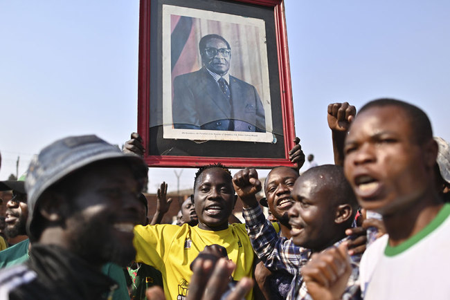 Youth carrying a portrait of Zimbabwe's late former president Robert Mugabe sing as they wait at the historic Rufaro stadium in the capital, Harare, for the arrival of his body where it will lay in state for members of the public to view on September 12, 2019. [Photo: AFP/Tony Karumba]