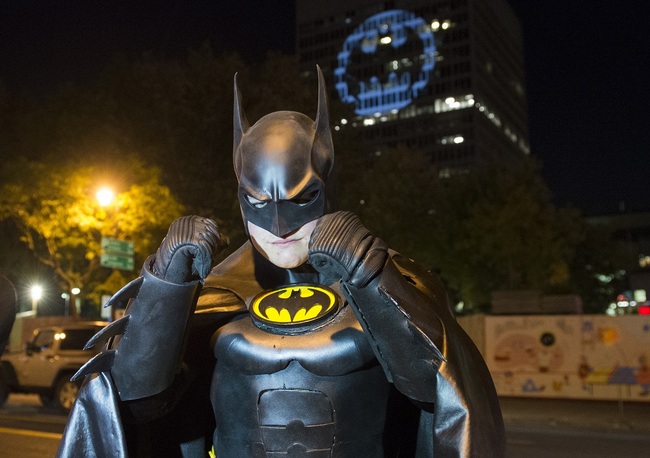 A man dressed in a Batman costume poses for a photo in front of the Batman signal projected onto a building to celebrate Batman Day in Montreal, Saturday, Sept. 21, 2019. [Photo: AP]<br>