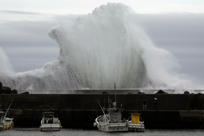 Men look at fishing boats as surging waves hit against the breakwater while Typhoon Hagibis approaches at a port in town of Kiho, Mie Prefecture, Japan, on Friday, Oct. 11, 2019. [Photo: AP/Toru Hanai]
