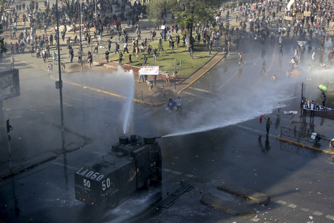 A police truck sprays water canons at protesters, amid ongoing demonstrations triggered by an increase in subway fares in Santiago, Chile, Monday, Oct. 21, 2019. [Photo: AP/Miguel Arenas]