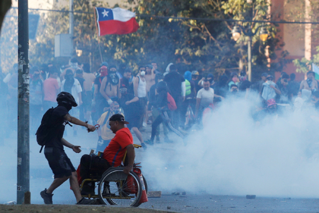 A demonstrator runs to assist a man in a wheelchair during a protest against Chile's government in Santiago, Chile November 5, 2019. [Photo: VCG]