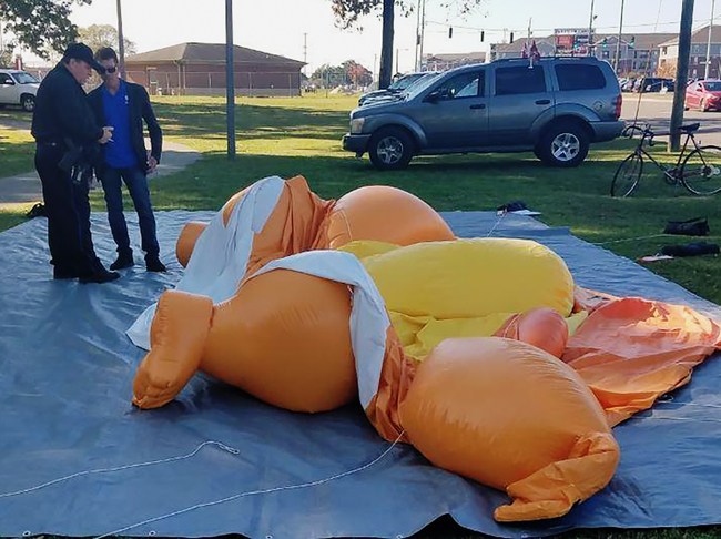 A responding officer and an unidentified man stands by a Baby Trump balloon deflated by someone at Monnish Park as people were protesting President Donald Trump's visit to an NCAA college football game between Louisiana State and Alabama playing nearby in Tuscaloosa, Ala., Saturday, Nov. 9, 2019. The towering Baby Trump protest balloon was knifed and deflated by someone unhappy with its appearance during Trump's trip to Alabama, organizers said. [Photo: AP/Stephanie Taylor/The Tuscaloosa News]