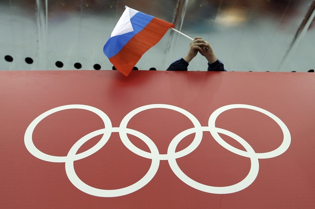 In this Feb. 18, 2014, file photo, a Russian flag is held above the Olympic Rings at Adler Arena Skating Center during the Winter Olympics in Sochi, Russia. [Photo: AP/David J. Phillip]