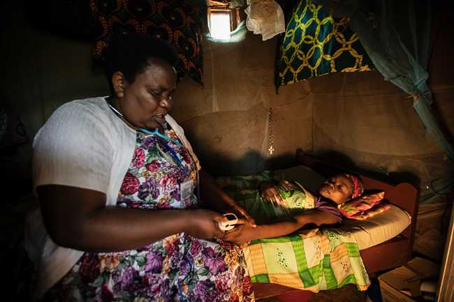 In this photo taken Tuesday, Nov. 5, 2019, palliative care nurse Madeleine Mukantagara, 56, left, uses a pulse-oximeter to check on the health of Vestine Uwizeyimana, 22, right, who has spinal degenerative disease and is taking oral liquid morphine for her pain, at her home in the village of Bushekeli, near Kibogora, in western Rwanda. [Photo: AP]