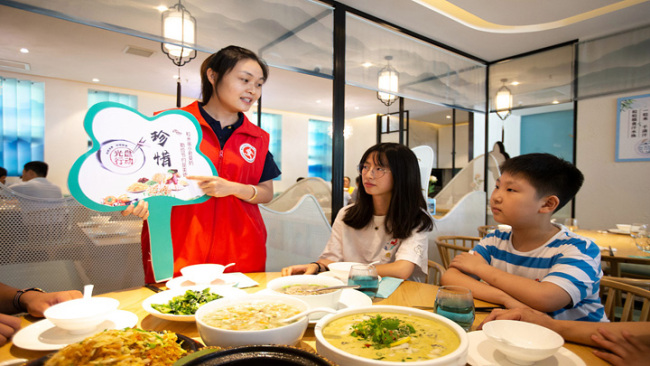 Snímek: Dobrovolnice navrhuje rodině, aby šetřila jídlo v komunitní restauraci v provincii Jiangsu (Ťiang-su) v Číně; 13. srpna 2020.