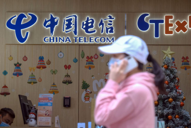 Chodec s ochrannou rouškou prochází kolem značení v obchodě China Telecom Corp. v čínském Hongkongu, 4. ledna 2021. / Getty