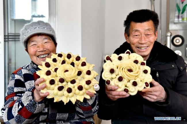 Chen Baicang (Čchen Paj-cchang, vpravo) a jeho manželka vystavují před lunárním Novým rokem v okrese Juancheng (Ťüan-čcheng) ve východočínské provincii Shandong (Šan-tung), 4. února 2021, knedlíky Huagao (Chua-kao) zdobené červenými datlemi. Lunární Nový rok patří k nejvýznamnějším svátkům v Číně a oslavné činnosti jsou rozmanité, včetně jídla. Když přichází lunární Nový rok, lidé po celé Číně připravují různá občerstvení, která, jak věří, jim přinesou štěstí. (Xinhua / Guo Xulei)