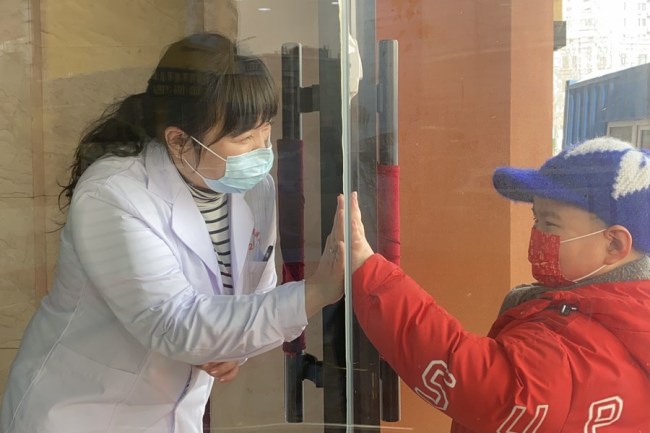 Zheng Yingying (Čeng Jing-jing), zaměstnankyně Lidové nemocnice, mluví se svým synem za skleněnými dveřmi na karanténním místě ve městě Harbin, hlavním městě provincie Heilongjiang (Chej-lung-ťiang) na severovýchodě Číny, 11. února 2021. (Xinhua / Yang Siqi)
